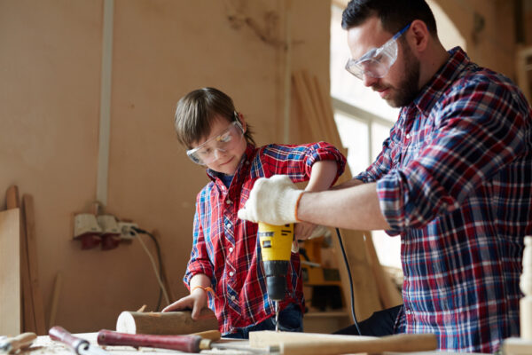 A Chicago handyman teaching a child how to use a power drill in a workshop.