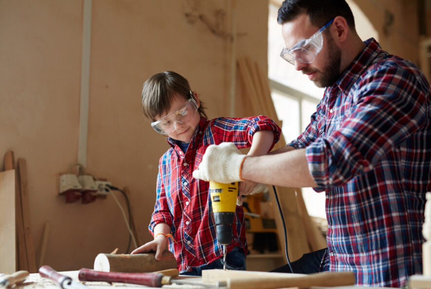 A Chicago handyman teaching a child how to use a power drill in a workshop.