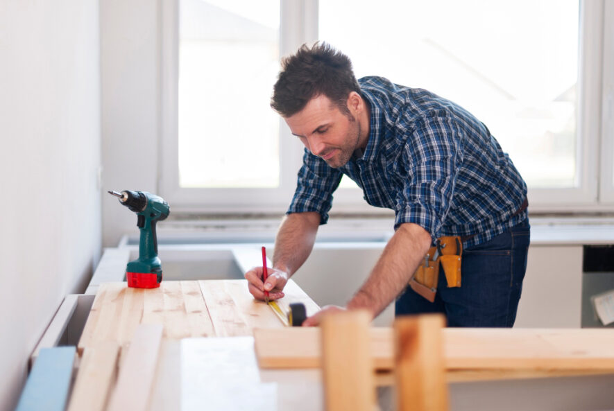 A carpenter measuring and marking a wooden board on a workbench with tools nearby, representing professional carpentry services Chicago.