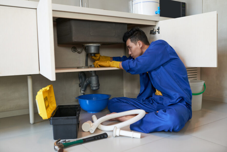 A plumber working under a kitchen sink with tools and equipment, illustrating “The Benefits of Professional Plumbing Maintenance.”